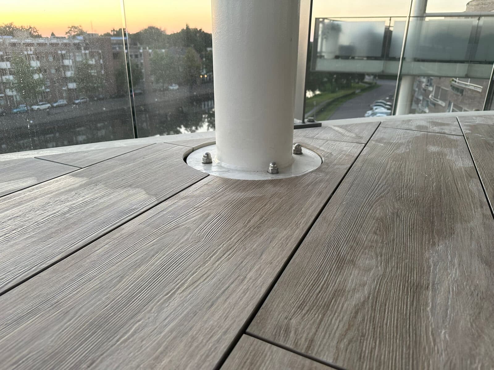 Houtlook tegels strak rondom een ronde pilaar gelegd, met bij zonsondergang uitzicht op het water