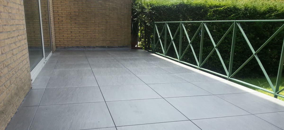 Balkon met grote grijze ITS tegels langs een groen hekwerk