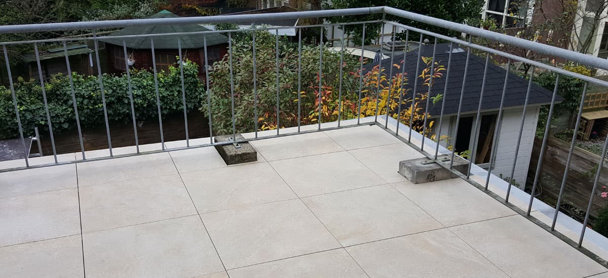 Dakterras met grote lichte keramische tegels achter een verzinkt hekwerk