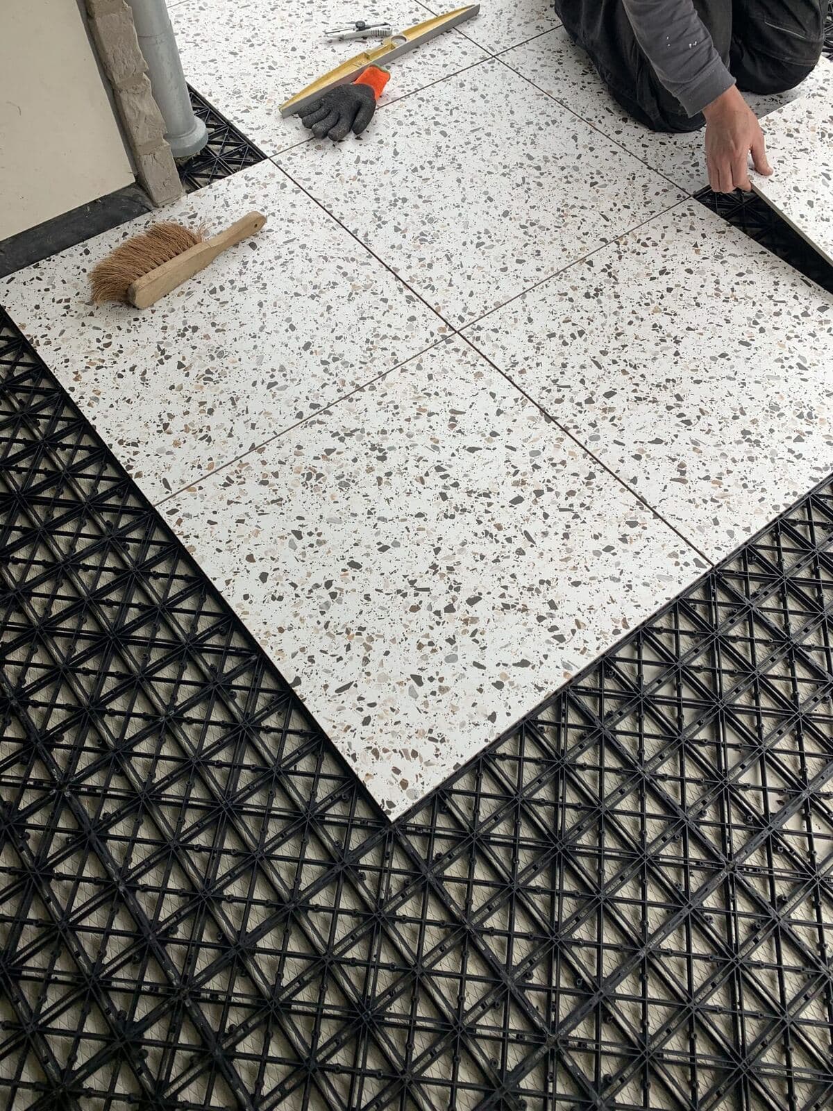 Een terrazzo tegel wordt met de hand in de zwarte ITS draagmat gelegd