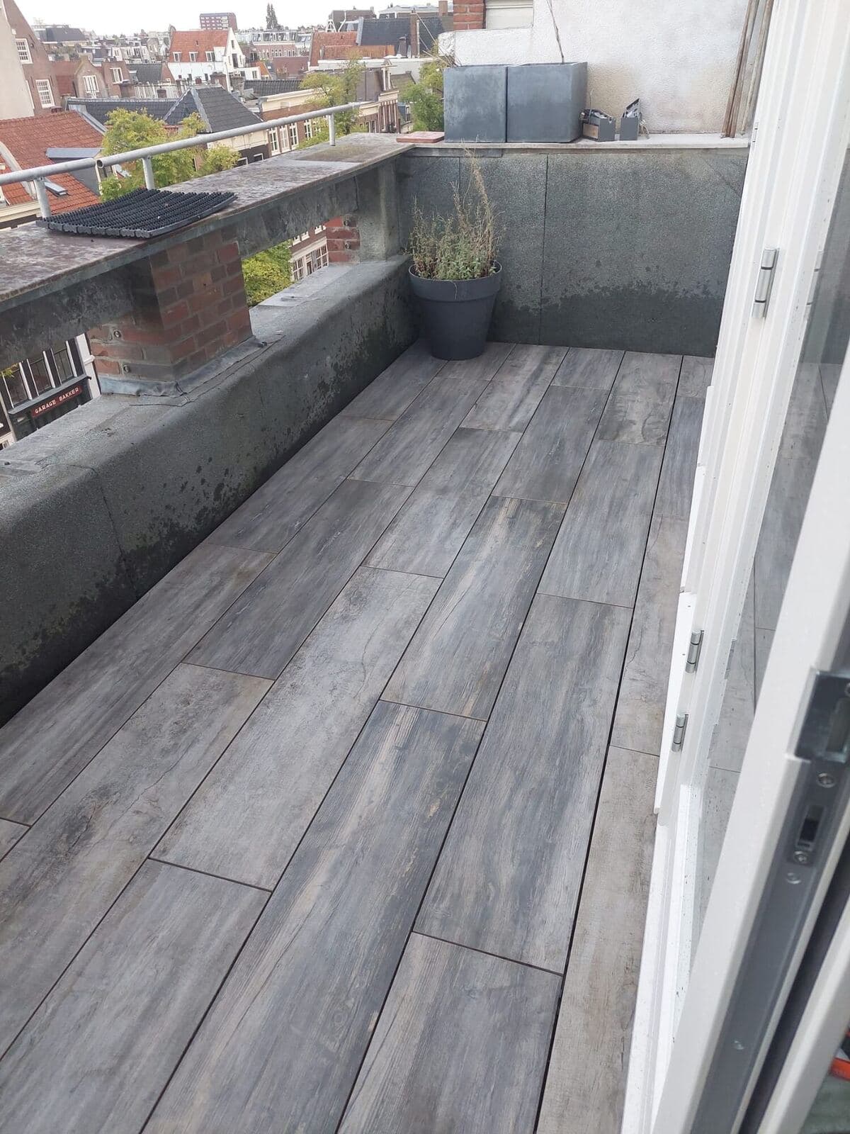 Smal balkon met lange grijze houtlook tegels en uitzicht over de daken van de stad